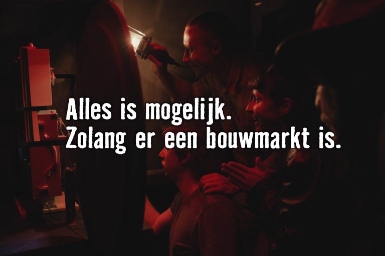 Groep mensen werkt in het donker met een zaklamp aan een project met de tekst Alles is mogelijk zolang er een bouwmarkt is