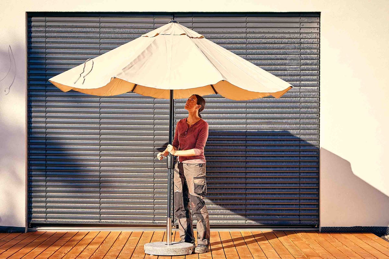 Vrouw onder een openstaande parasol met voet op een houten terras