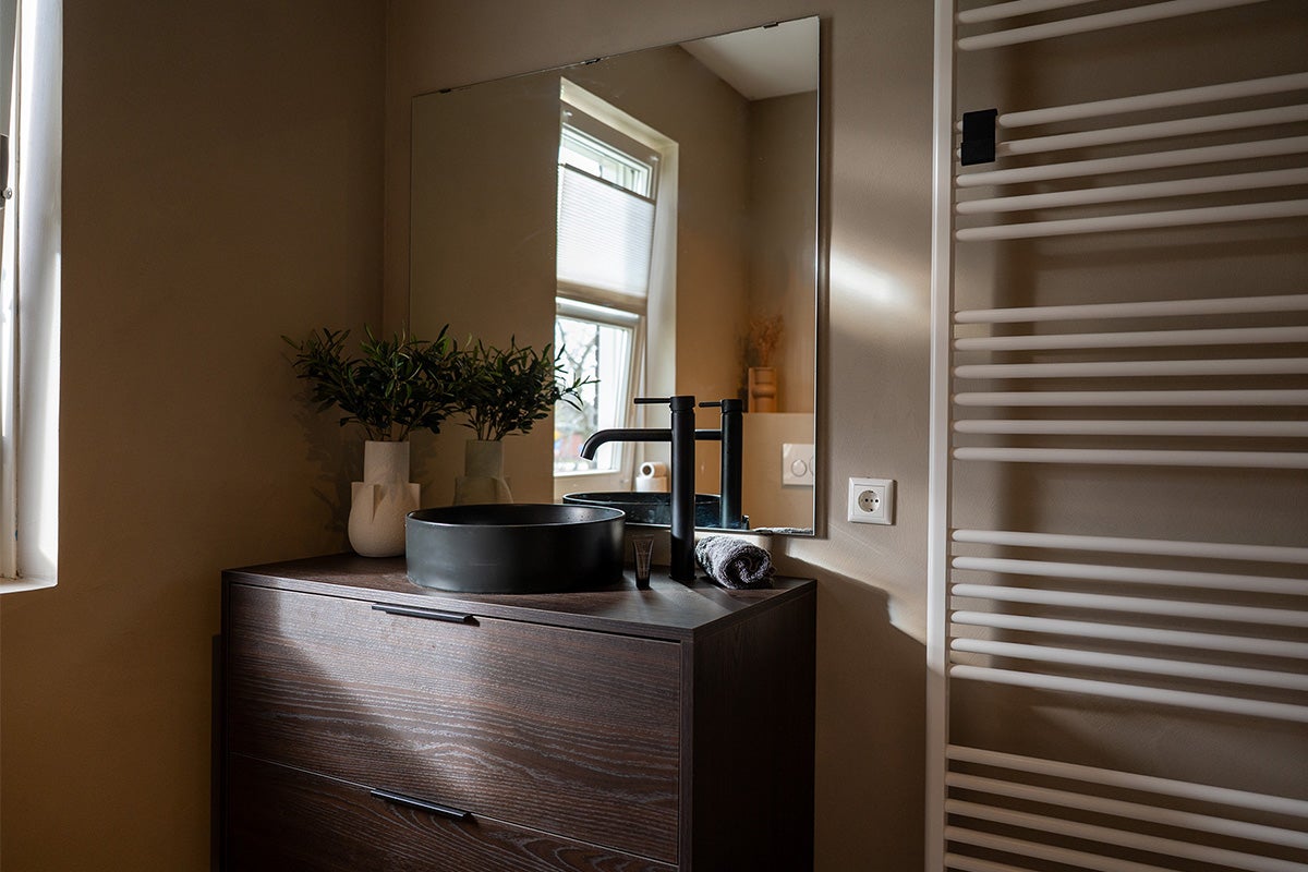 Moderne badkamer met donker wastafelonderstel, zwarte opzetwastafel, spiegel en radiator