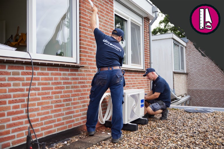 Twee ambachtslieden installeren een airconditioner op een gebouw.