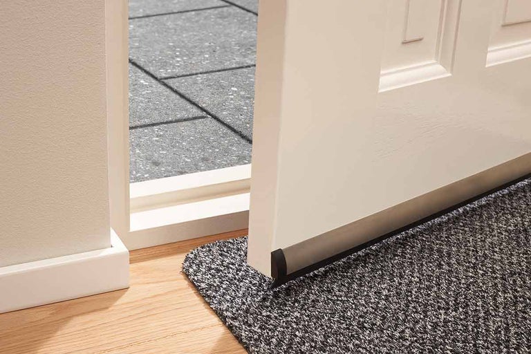 Detailweergave van een deur met deurafdichting en een deurmat in de entree