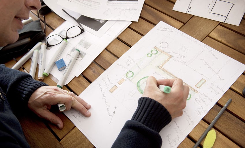 Een man ontwerpt een tuinplan met markers op een houten tafel, waarop verschillende tuinbouw elementen staan.
