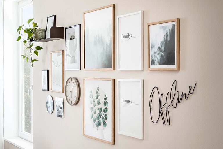 Moderne fotowand met fotolijsten van hout en wit, een wandklok, een plankje met plant en een metalen Offline-tekst.