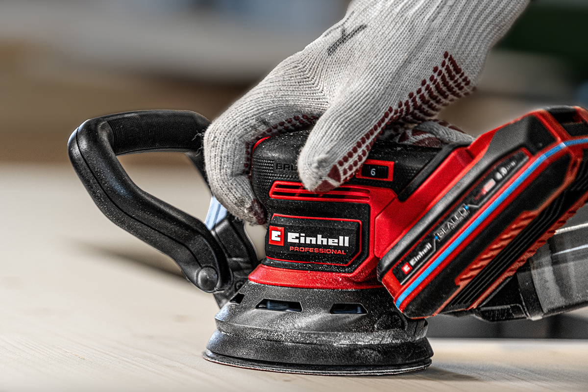 Einhell snoerloze excenterschuurmachine Professional in gebruik op een houten oppervlak met een werkhandschoen.