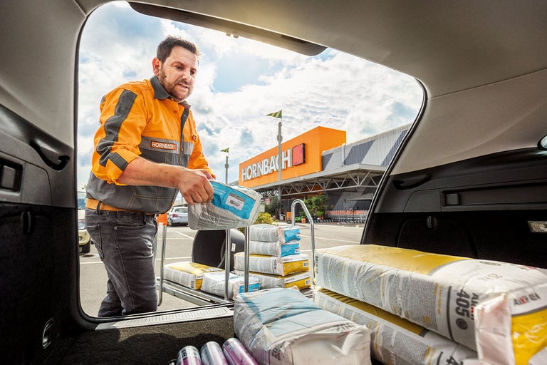 Een Hornbach-medewerker laadt bouwmateriaal in de kofferbak van een auto voor een Hornbach-winkel.