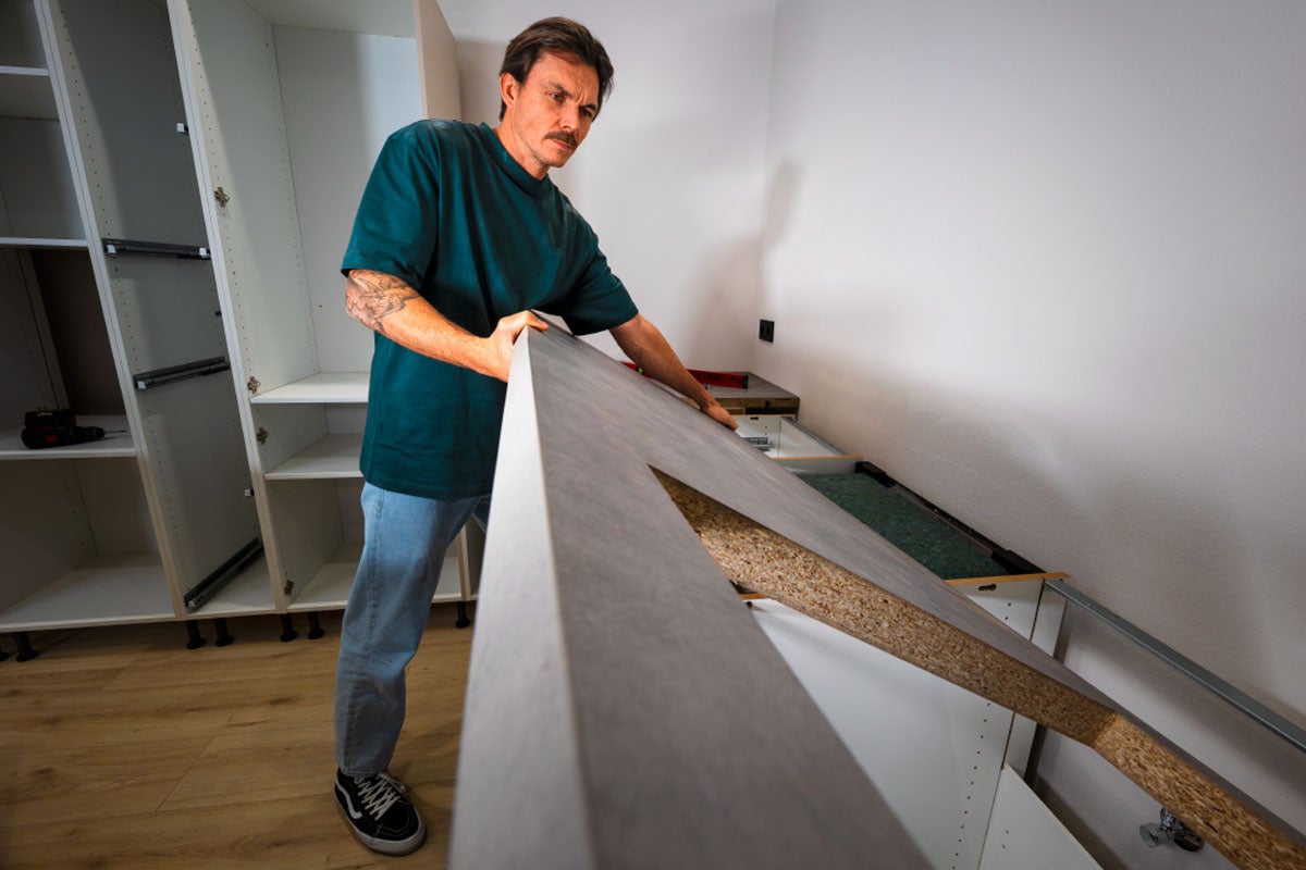 Een vakman monteert een grijs keukenwerkblad op keukenkastjes in een keuken die wordt opgebouwd.