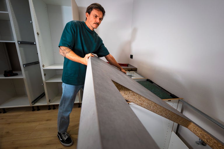 Een vakman monteert een grijs keukenwerkblad op keukenkastjes in een keuken die wordt opgebouwd.