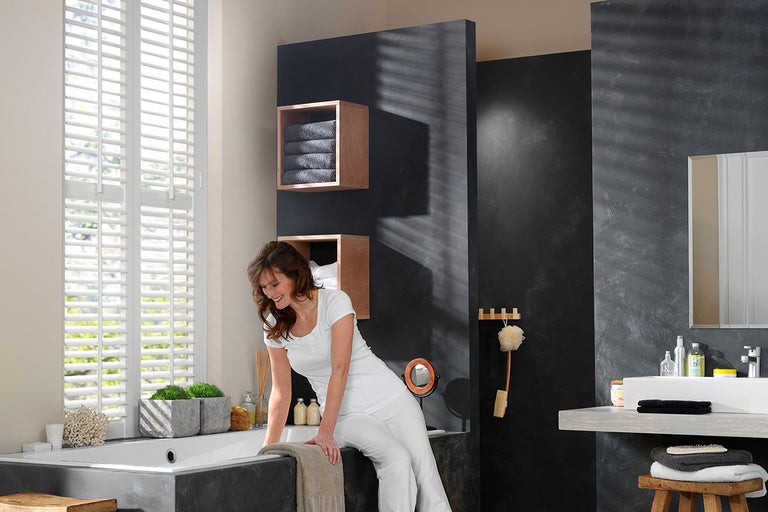 Badkamer met ligbad, jaloezieën, wastafel en decoratieve planken