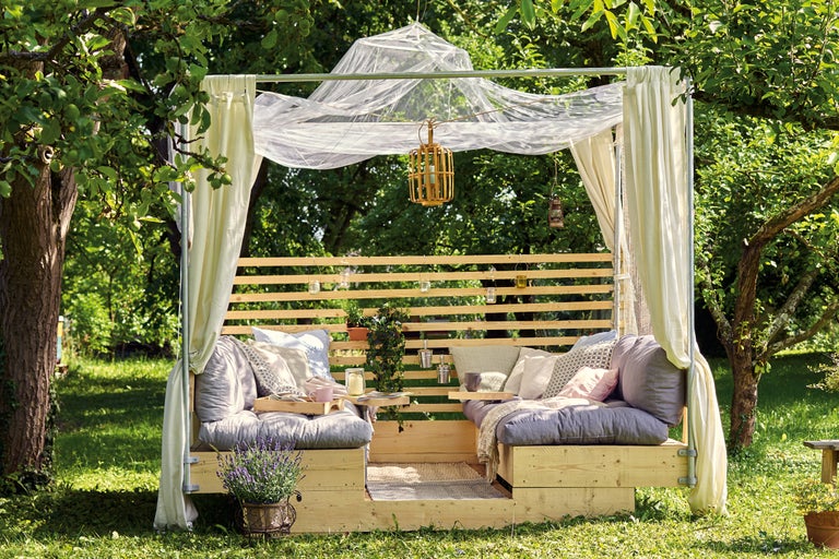 Tuinzitgroep met houten frame, gordijnen en decoratie onder bomen