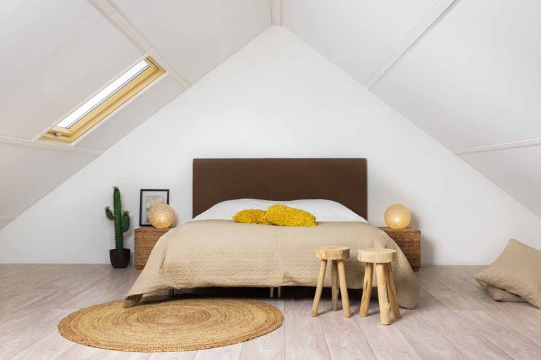 Slaapkamer op zolder met bed, dakraam en houten krukken