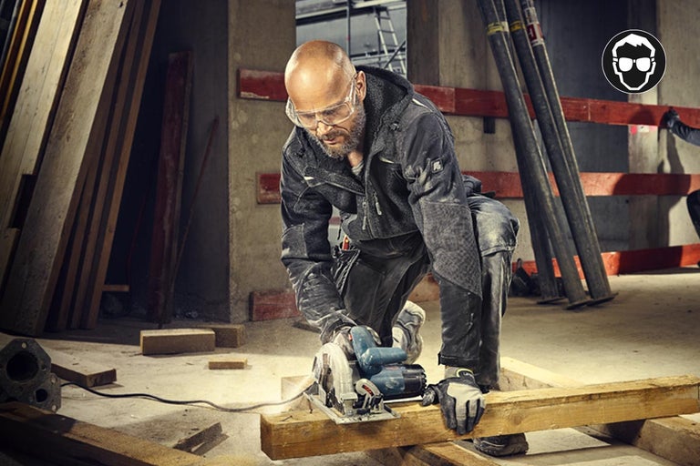Man zaagt hout met een cirkelzaag, hij draagt beschermende kleding