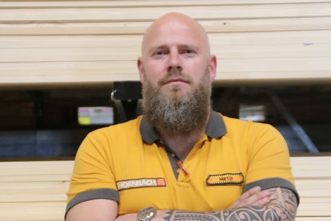 Hornbach medewerker met baard en tatoeages draagt een poloshirt met Hornbach Logo voor houten planken.