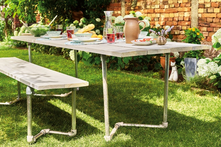 Tuinscene met gedekte houten tafel en zitbank op een gazon