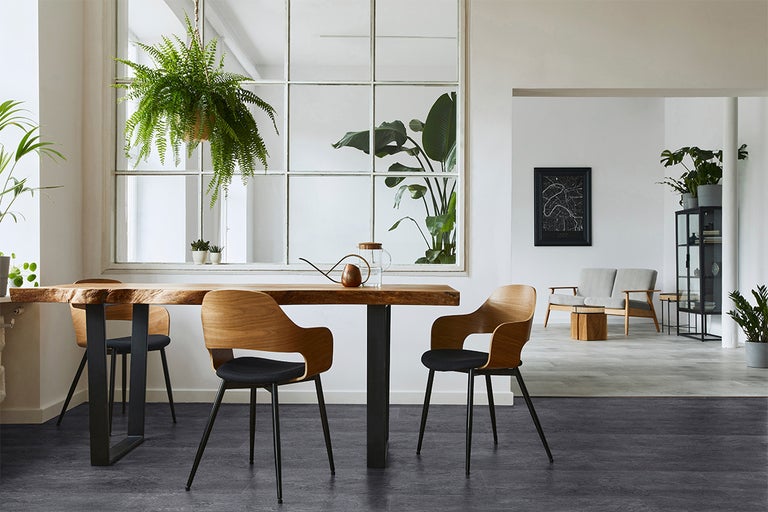 Moderne eetruimte met donkere vloerbedekking, een boomstamtafel, houten stoelen en diverse kamerplanten in een lichte kamer.