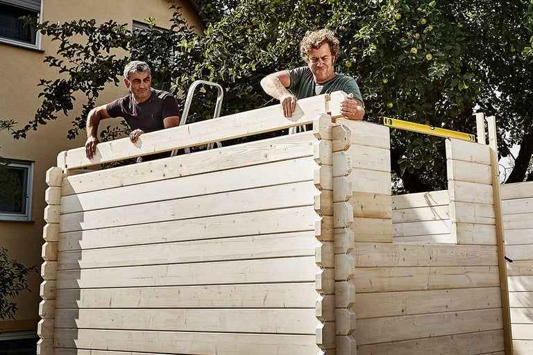 Twee mannen bouwen een houten tuinhuis met een waterpas