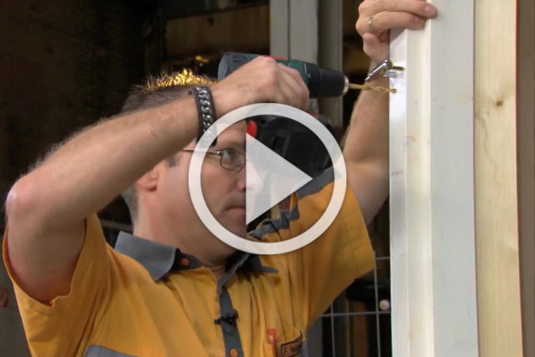 Een persoon boort met een accuschroevendraaier een scharnier aan een deur.