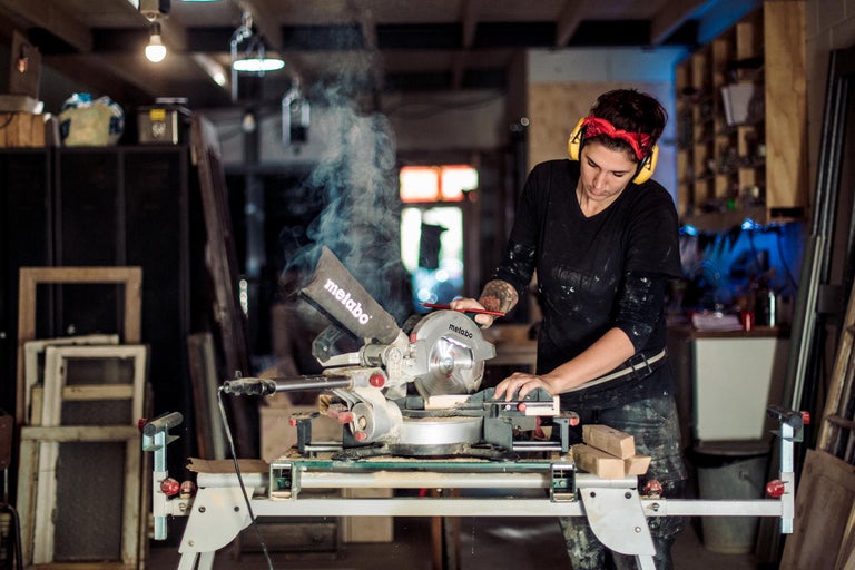 Een vrouw werkt met een Metabo verstekzaag in een werkplaats en draagt daarbij gehoorbescherming.
