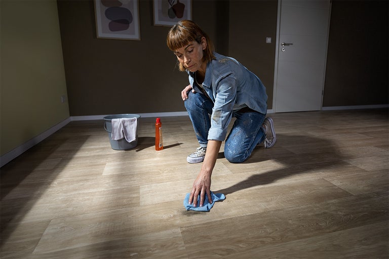 Vrouw maakt vloer schoon met emmer en schoonmaakmiddel in een kamer