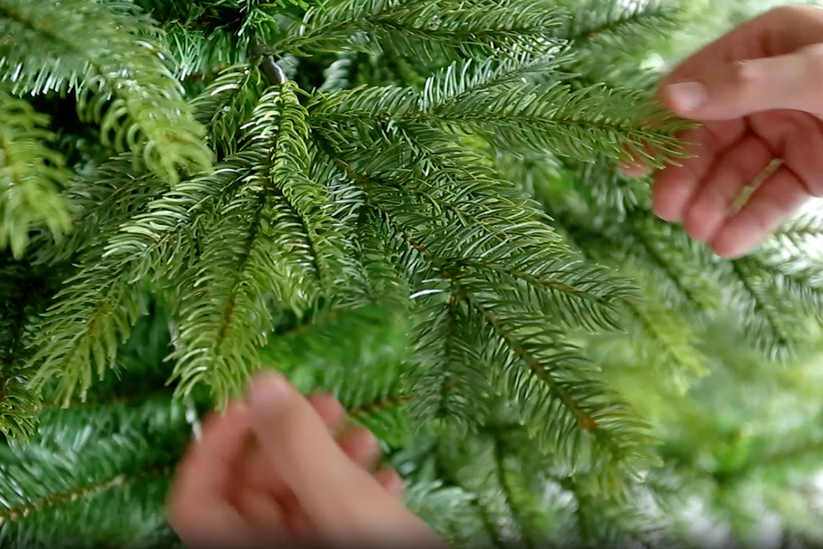 Detailopname van een kunstkerstboom met groene naalden en handen.