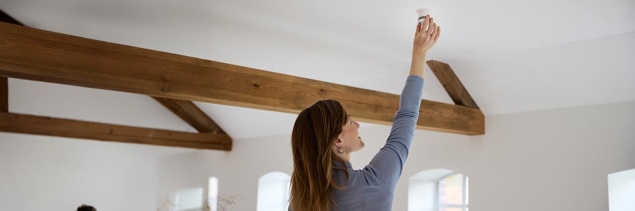 Vrouw installeert rookmelder in een lichte ruimte met houten balken