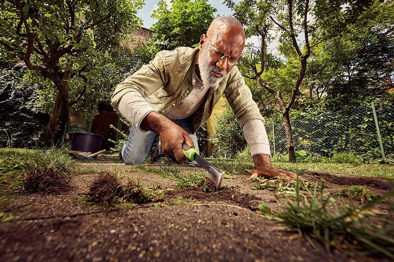 Een man wiedt onkruid in een tuin met een onkruidsteker.