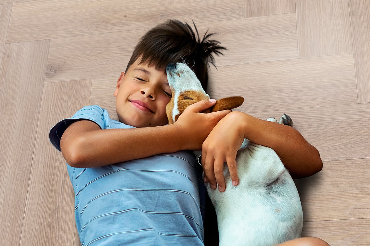 Kind omhelst een kleine hond op een lichte vloer met visgraatmotief in houtlook.