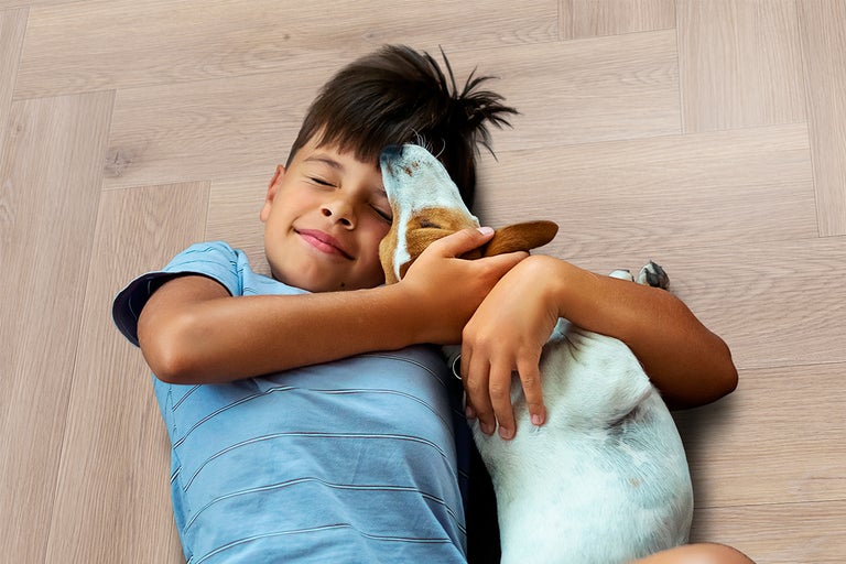 Kind omhelst een kleine hond op een lichte vloer met visgraatmotief in houtlook.