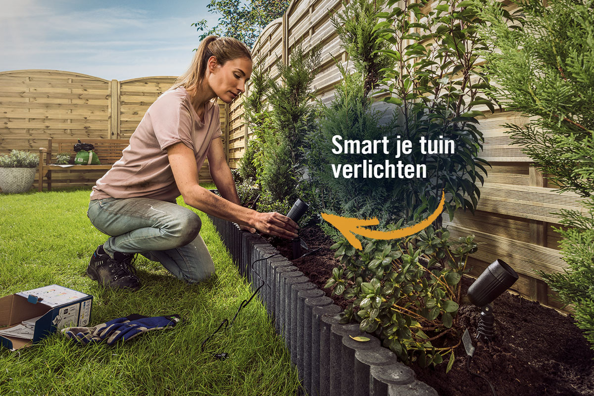 Een vrouw installeert tuinverlichting in een tuin met gazon en planten.