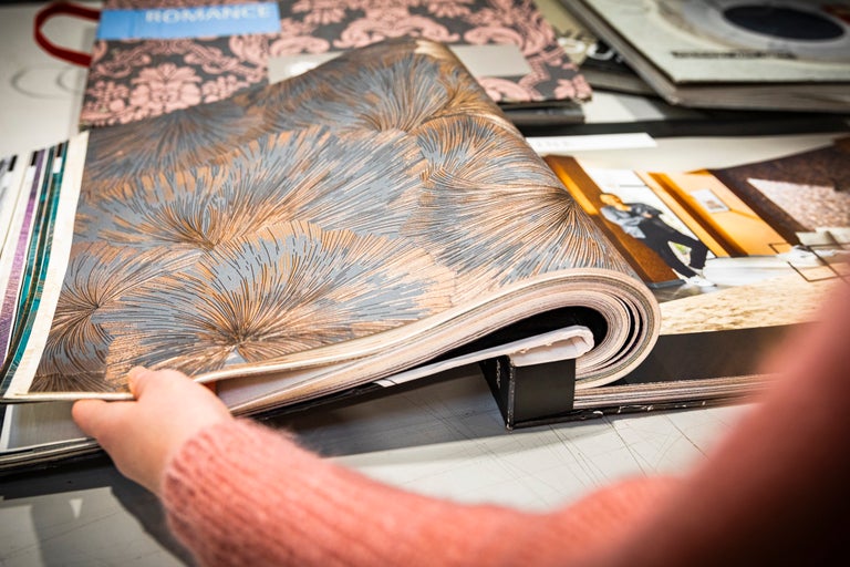 Een persoon bladert door een behangstalenboek met een bloemmotief.