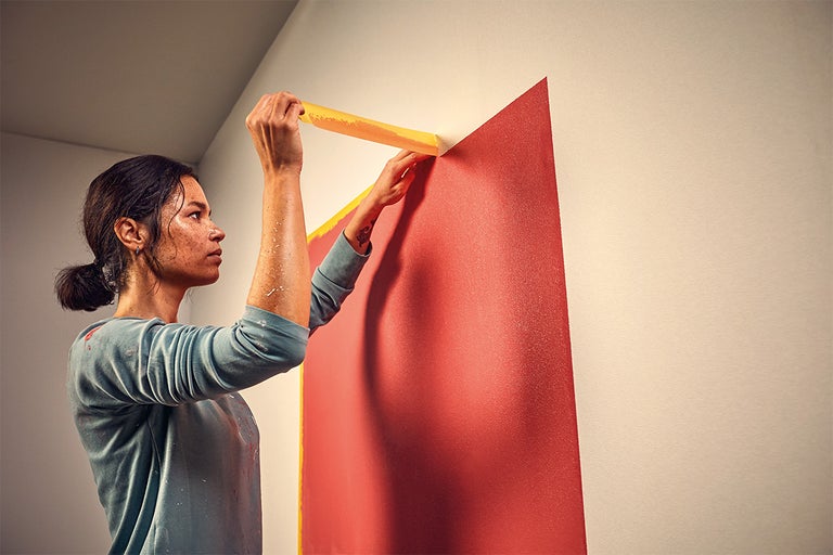 Een persoon plakt schilderstape op een muur om een verfgebied af te bakenen.