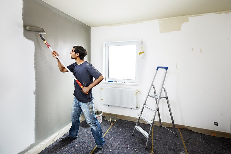 Man schildert muur met verfroller in een te renoveren kamer.