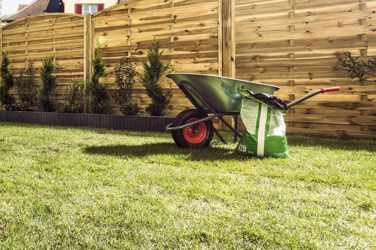 Tuinlandschap met houten schutting, kruiwagen en zak potgrond op gazon