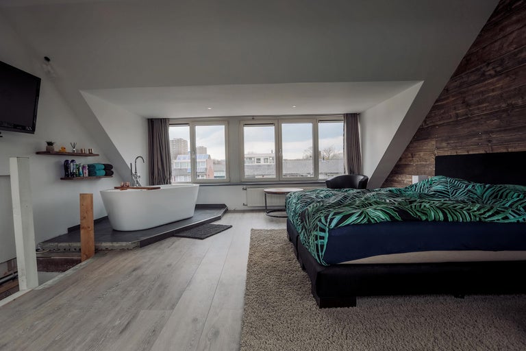 Lichte kamer met bad, bed en houten wand