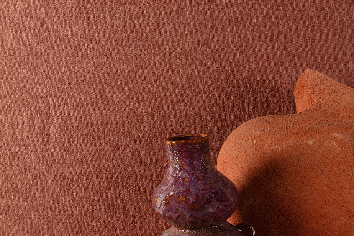 Terracotta behang met fijne geweven textielstructuur, getoond met een paarse keramische vaas en een aardewerken object.