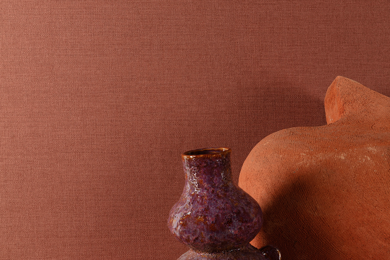 Terracotta behang met fijne geweven textielstructuur, getoond met een paarse keramische vaas en een aardewerken object.