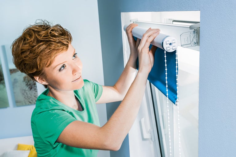Vrouw monteert een rolgordijn aan het raam