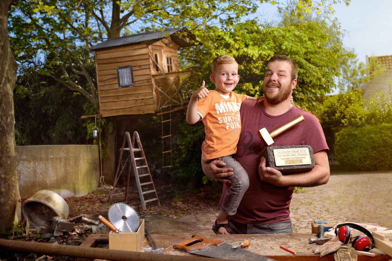Vader houdt zijn zoon vast voor een boomhut met gereedschap en een award met het Hornbach logo.