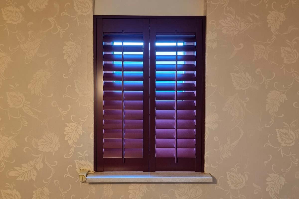 Raam met shutters voor een behang met bloemmotief als zonwering.