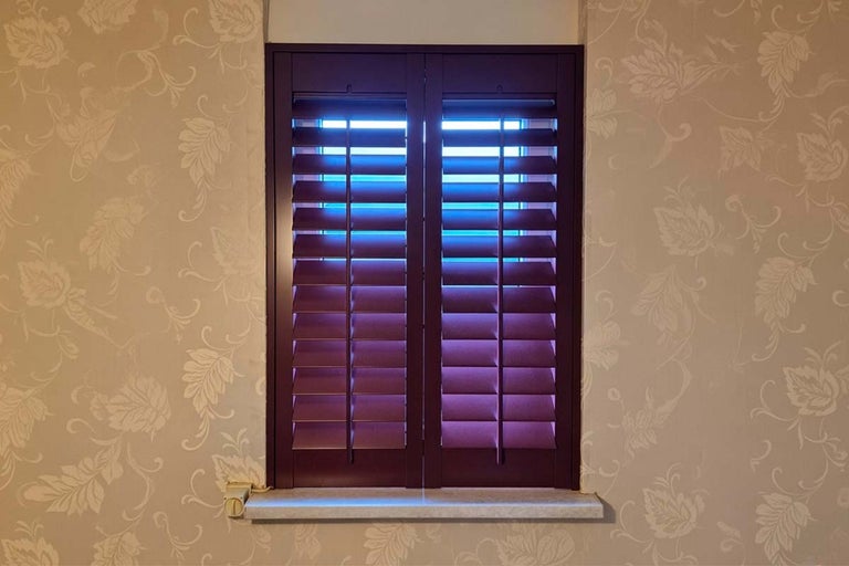 Raam met shutters voor een behang met bloemmotief als zonwering.