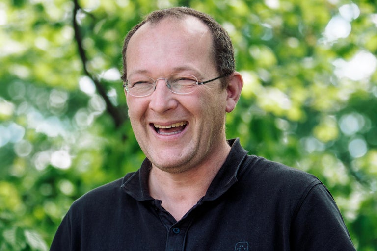 Portret van een lachende man met bril tegen een groene achtergrond