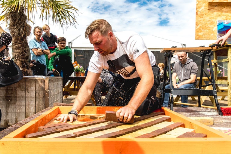 Een persoon legt straatstenen in een kader, omringd door toeschouwers.