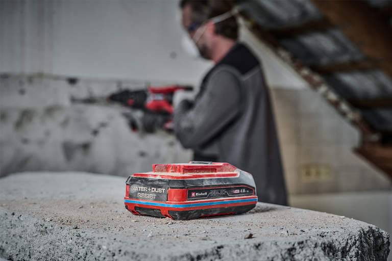 Einhell accu 4,0 ampère-uur met water- en stofbestendigheid op een betonblok op een bouwplaats met een vakman op de achtergrond.