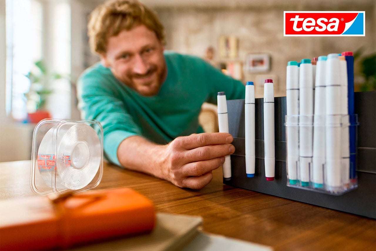 Scene met man, dubbelzijdige tape en markers op een tafel, Tesa Logo