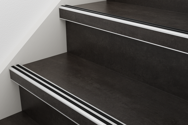 Trapneusprofiel in zilver met zwarte antislipstrips op donkere treden met steeneffect.
