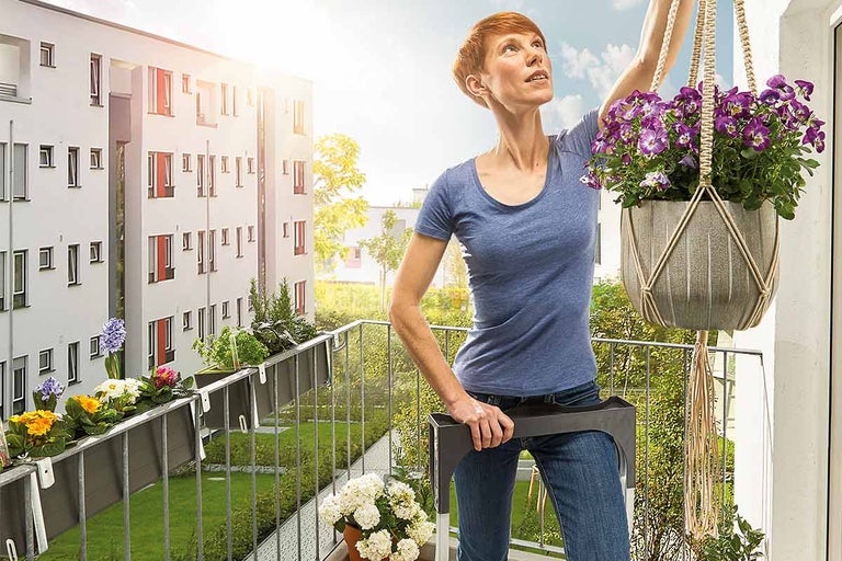 Vrouw op een balkon met balkonbakken en een hangende plantenmand met bloemen