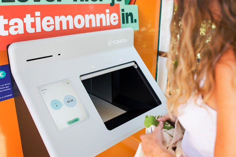 Vrouw gebruikt een Tomra flessenautomaat om statiegeldflessen in te leveren