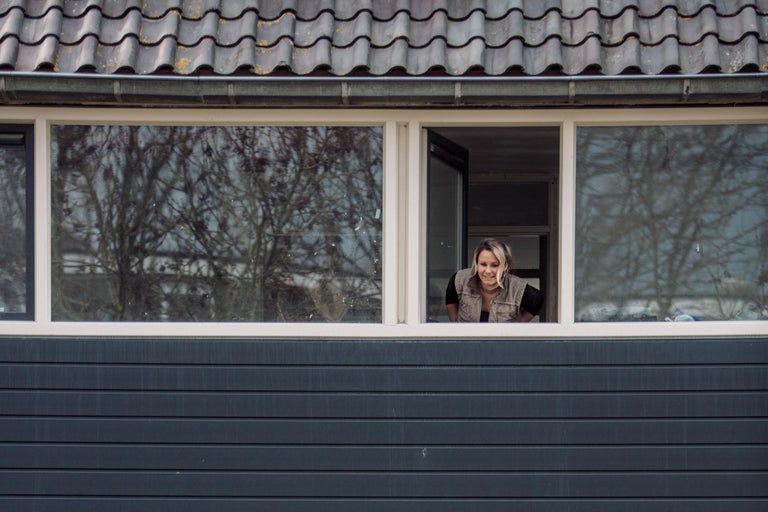 Vrouw kijkt uit het raam van een huis met een pannendak