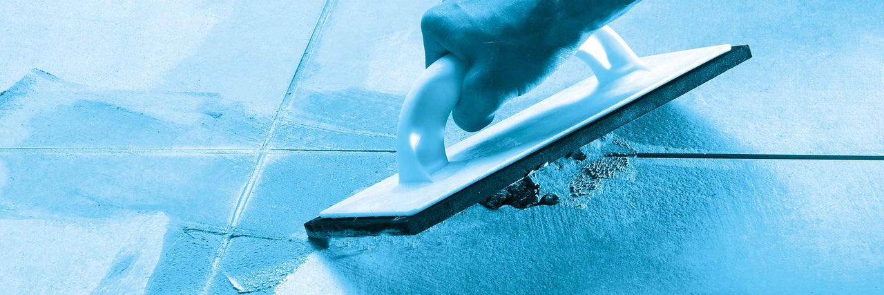 Tegelzetter met voegrubber bij het voegen van tegels