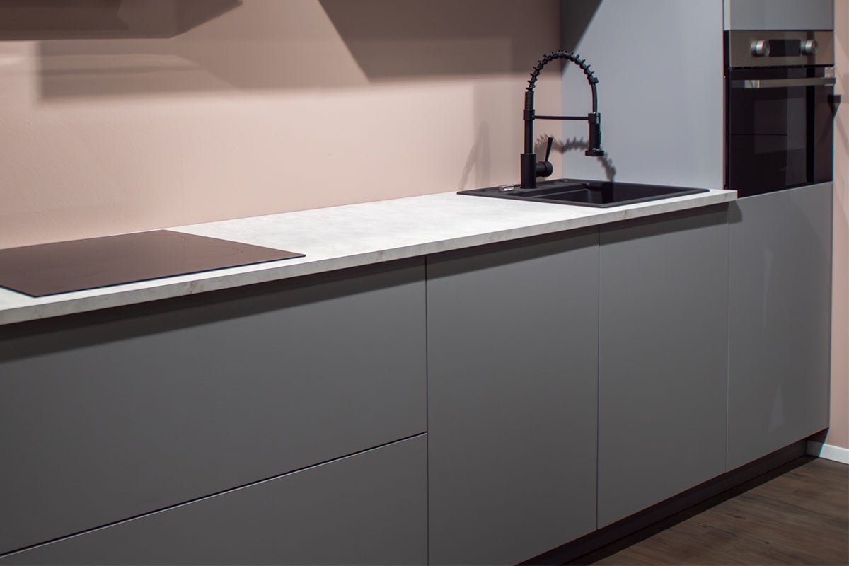 Moderne keuken met grijze kasten, licht werkblad met steeneffect, zwarte spoelbak met spiraalveerkraan, kookplaat en inbouwoven.