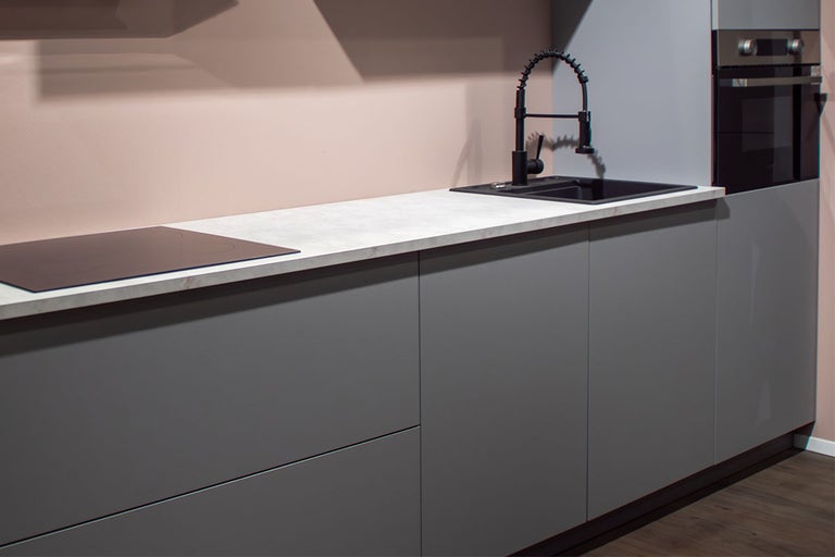 Moderne keuken met grijze kasten, licht werkblad met steeneffect, zwarte spoelbak met spiraalveerkraan, kookplaat en inbouwoven.
